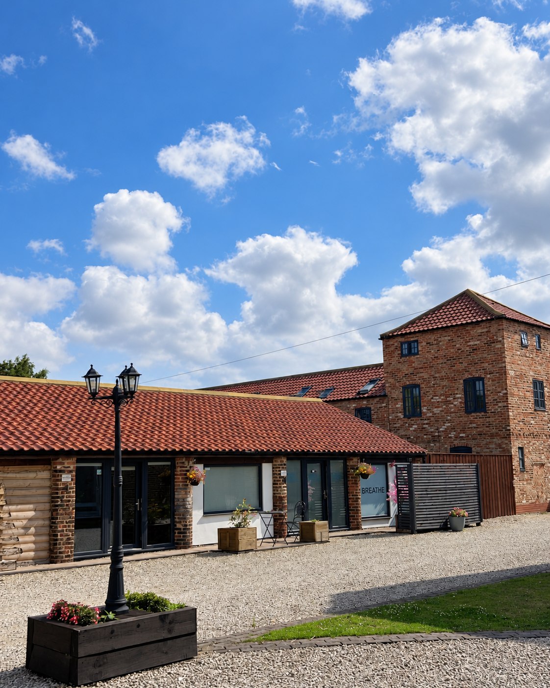 The Breathe Manor Farm exterior, with red-tiled roofs, a brick tower and a gravel courtyard.