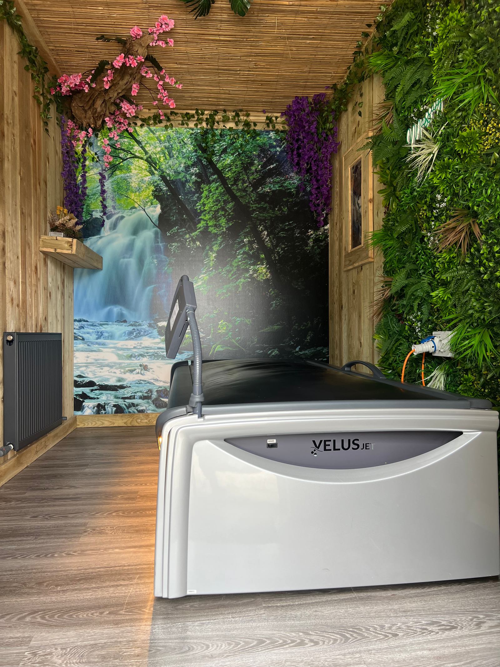 The hydro massage bed in a timber-lined room with greenery and a waterfall mural.